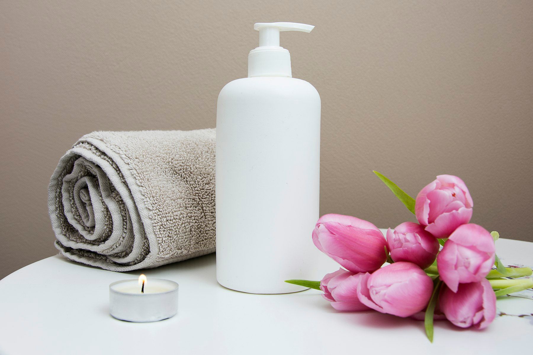 Toalla blanca, dispensador y flores en una cabina de spa